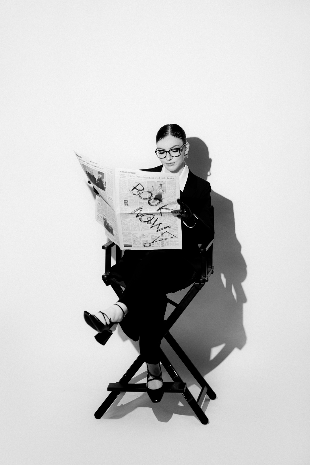 Lisa Marie liest eine Zeitung mit der Aufschrift Book Now